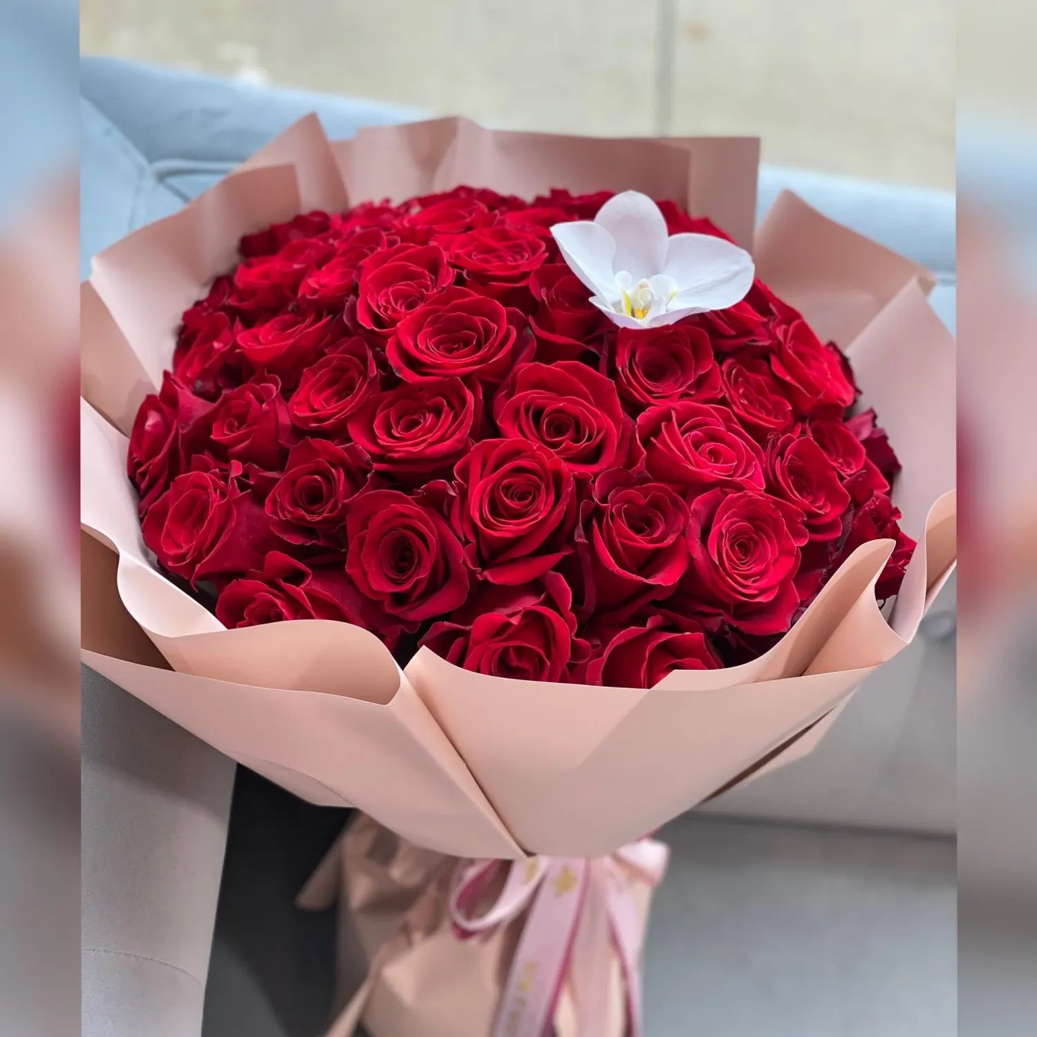Bouquet of 100 red roses with a white orchid in pink paper wrapping.